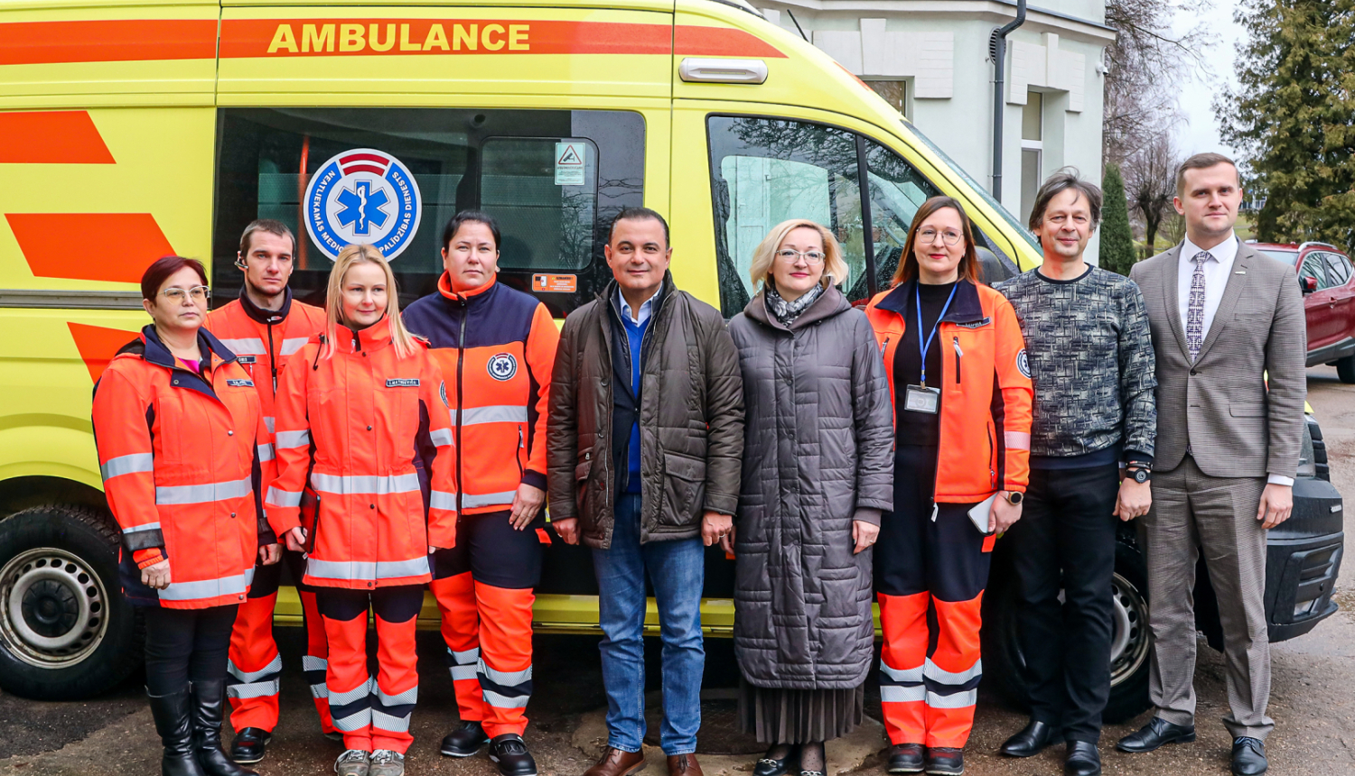 mediķi un politiķi stāv pie ātras palīdzības auto